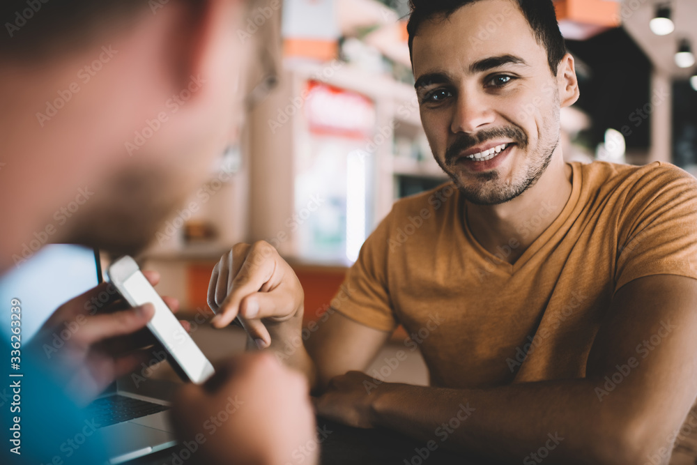 Aufkleber portrait of cheerful caucasian man pointing on smartphone with mock up screen sitting with friend in