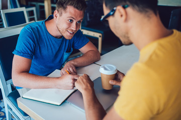 Fototapeta premium Cheerful male writing note doing project with partner in cafe