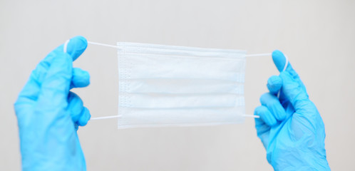 Fototapeta premium medical mask in the hands of a doctor in blue rubber gloves close-up on a light background. Hygiene, coronavirus, covid-19, airborne.