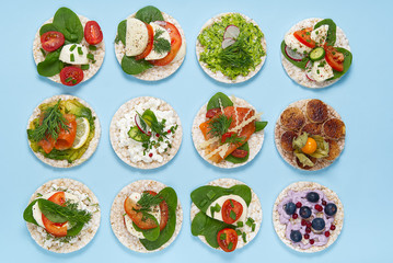 set of rice cakes on light blue background. healfy food rice cake sandwich isolated on light blue background. Rice cakes with Basil, tomatoes, avacado, cheese and red trout or salmon fish, mozerella