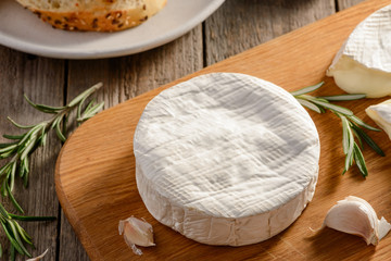Closeup on a whole wheel of Brie cheese, garlic and rosemary