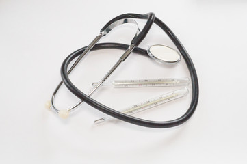 Black stethoscope and two analog mercury thermometers on a white background