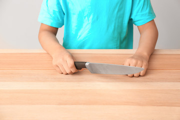 Little African-American boy with knife at table. Child in danger