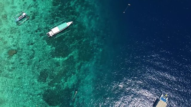 some boats filmed from the top with the drone, on the shore of the ocean near a beach in the tropical area, a blue and transparent water. Pleasant rest on the ocean.
