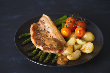 Roast pork chop with vegetables on black plate. horizontal image