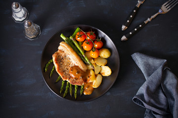 Roast pork chop with vegetables on black plate. Overhead horizontal image