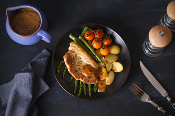 Roast pork chop with vegetables on black plate. Overhead horizontal image