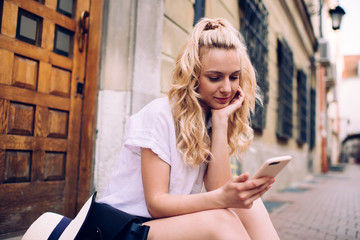 Positive woman texting on smartphone while sitting at staircase at street