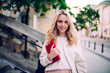 Smiling female student holding book on street