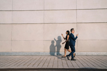 Businesswoman and businessman walking past each other and text messaging on cellphones