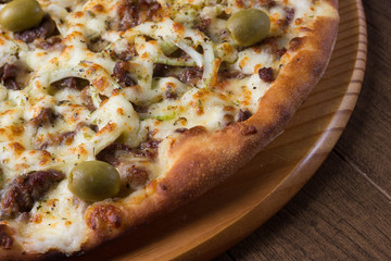 Meat pizza on wooden board. Made with Mozzarella, picanha meat, onion, cheese, tomato sauce and olives. Filet Steak, meat. Macro photo showing edge of wooden board.