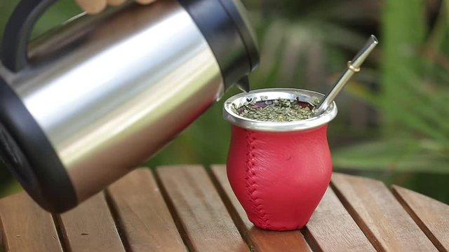 Man making yerba mate tea. Close up pouring hot water into traditional Mate cup. Kettle pours hot water into a red mate to make a delicious steaming yerba mate infusion, a traditional South American, 
