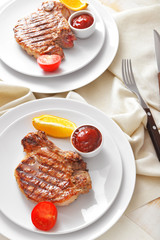 Plates with cooked pork steaks and sauce on table