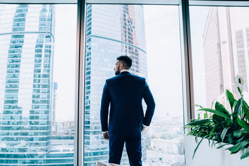Serious smart businessman standing at window in office