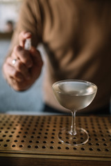 Bartender preparing cocktail based on gin, birch juice cordial and spraying essential oil of frankincense into a glass with cocktail.