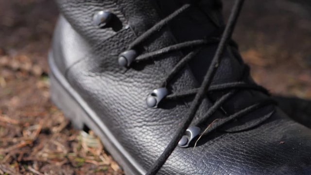 Descending close up of a military personnel lacing up their leather boots to prepare for work