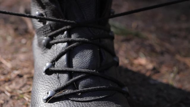 Close up of a caucasian person tightening and lacing up a pair of high-rise leather combat boots