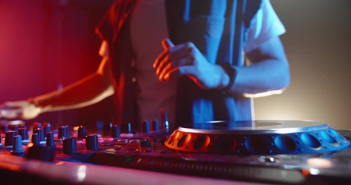 Cool dj standing at a mixer controller composing a dance music list, dancing while spotted by nightclub colorful lights - nightlife concept 4k footage