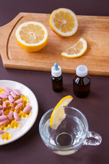 Tablets and fish oil in a plate and a transparent Cup with lemon on a brown background, cold and flu treatment
