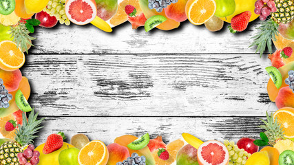 Creative photo of many different exotic tropical bright fruits frame with shadows on old grunge vintage wooden background. View from above. Bright summer fruit pattern with copy space.