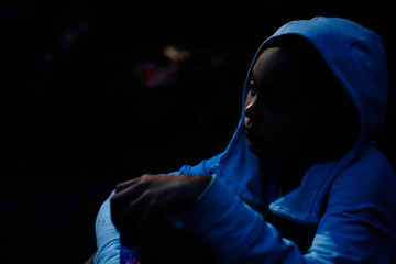 Sad girl in hoodie sitting in the dark with face lit by moonlight