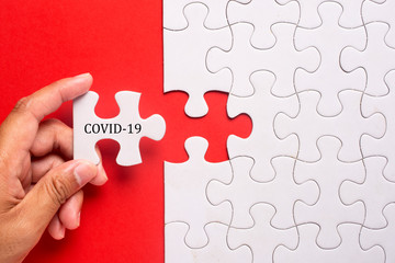 Hand holding piece of white puzzle on blue background with word COVID-19. Coronavirus pandemic prevention social distance and self-quarantine.