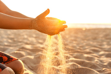 Little boy playing with sand on the beach at sunset in California, closeup of hands at natural...