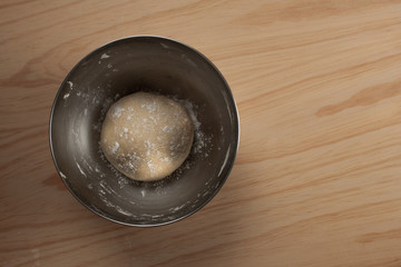 Overhead view of a ball of pizza dough with flour in an iron bowl on a wooden table