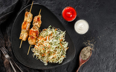 Grilled meat skewers with salad of cabbage and ketchup sauce on black stone background. Hot fast food dish, top view