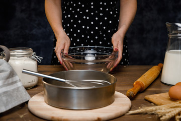 The confectioner prepares the dough, bread, cakes. Preparation and work with flour, eggs, milk and ingredients. Delicious food, recipes, cooking, gastronomy, on a dark background and wooden table.