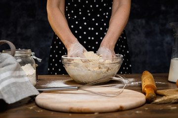 The confectioner prepares the dough, bread, cakes. Preparation and work with flour, eggs, milk and ingredients. Delicious food, recipes, cooking, gastronomy, on a dark background and wooden table.