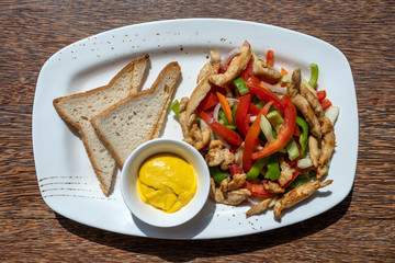 Roasted chicken fillet with vegetables and bread on a white plate, closeup