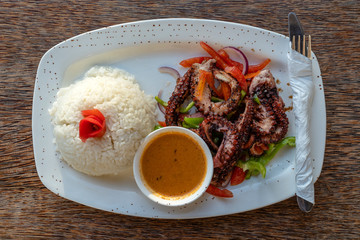 Fried octopus tentacles with white rice on a plate, close up