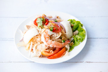 Spicy Vermicelli Seafood Salad with vegetable ingredient on wood white background, Thai food Street food Concept.Top View