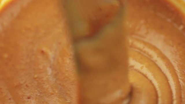 Stirring creamy peanut butter in jar with kitchen knife, close-up, 4K
