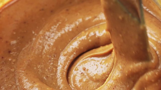 Stirring creamy peanut butter in jar with kitchen knife, close-up, 4K
