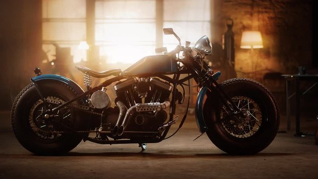 Custom Bobber Motorbike Standing in an Authentic Creative Workshop. Vintage Style Motorcycle Under Warm Lamp Light in a Garage. Profile View.