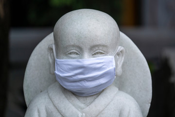 Portrait of buddhist statue wearing a face mask, closeup. Concept flu epidemic, coronavirus, dust...