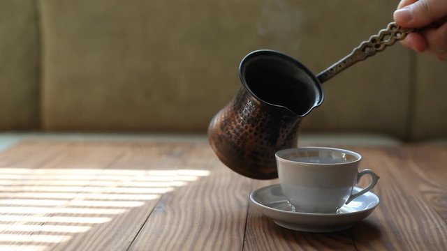 Barista pours coffee into a cup. A steaming cup of Turkish coffee. Coffee break.