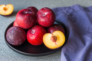 Red organic plums against grey stone background