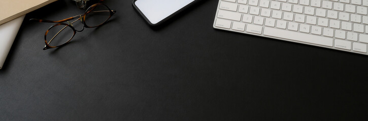 Top view of dark workspace with computer keyboard, smartphone, eyeglasses and copy space