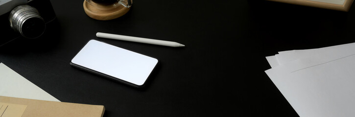 Cropped shot of dark concept workspace with mock-up smartphone, stylus, supplies and copy space