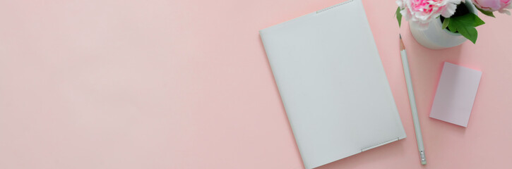 Top view of creative home office with diary notebook on pink table