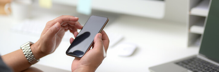 Cropped shot of male entrepreneur using smartphone while sitting at minimal workspace