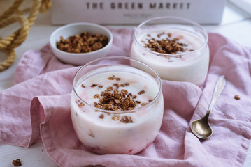 Bowl of granola with natural yogurt and raspberries. On a white wooden background and a pink fabric napkin. Copper spoon.