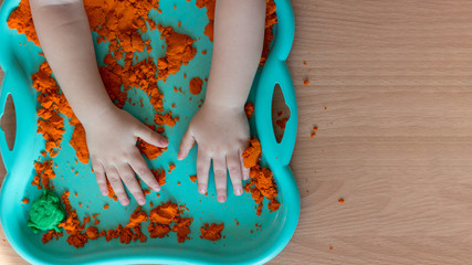 A child plays with kinetic sand. Child's hands in orange sand close-up in a green sandbox. Copy...