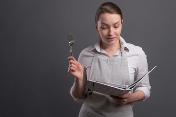 Girl chef with a recipe book, and cooking appliances on a gray background and space. Recipe book,...