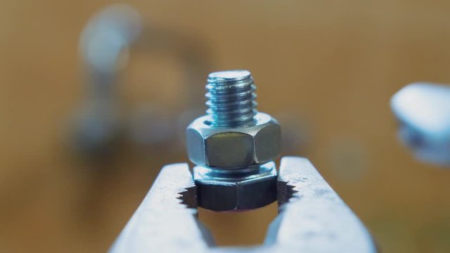 Counterclockwise of a wrench turning a bolt off a screw held by pliers, close up