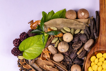 Macro shot of whole spices and green herbs with a wooden spoon containing yellow tablets. Alternative medicine concept