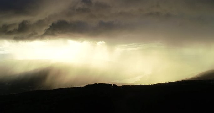 Aerial view of epic dramatic storm and rain over idyllic beautiful valley and mountains during sunset.